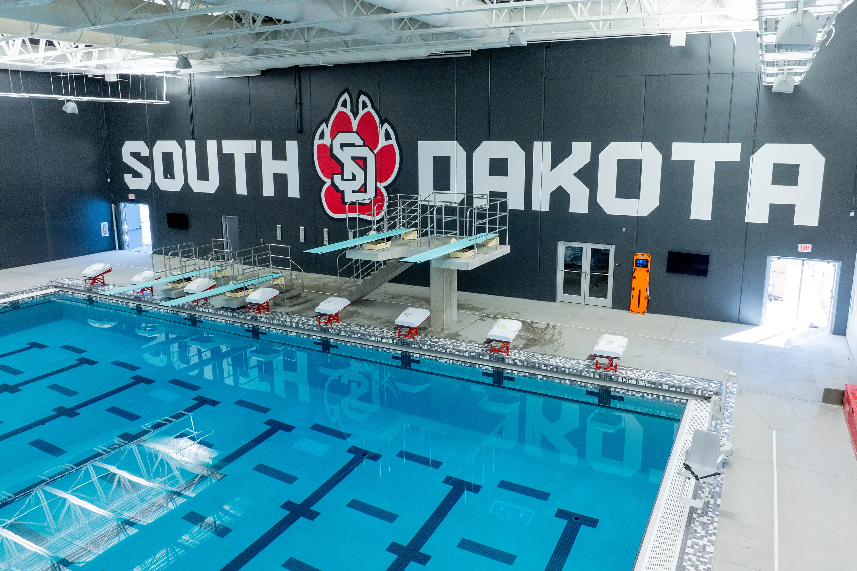 Usd Natatorium Wellness Center 20 Wide shot of South Dakota swim and dive wall graphics with diving platforms in view.