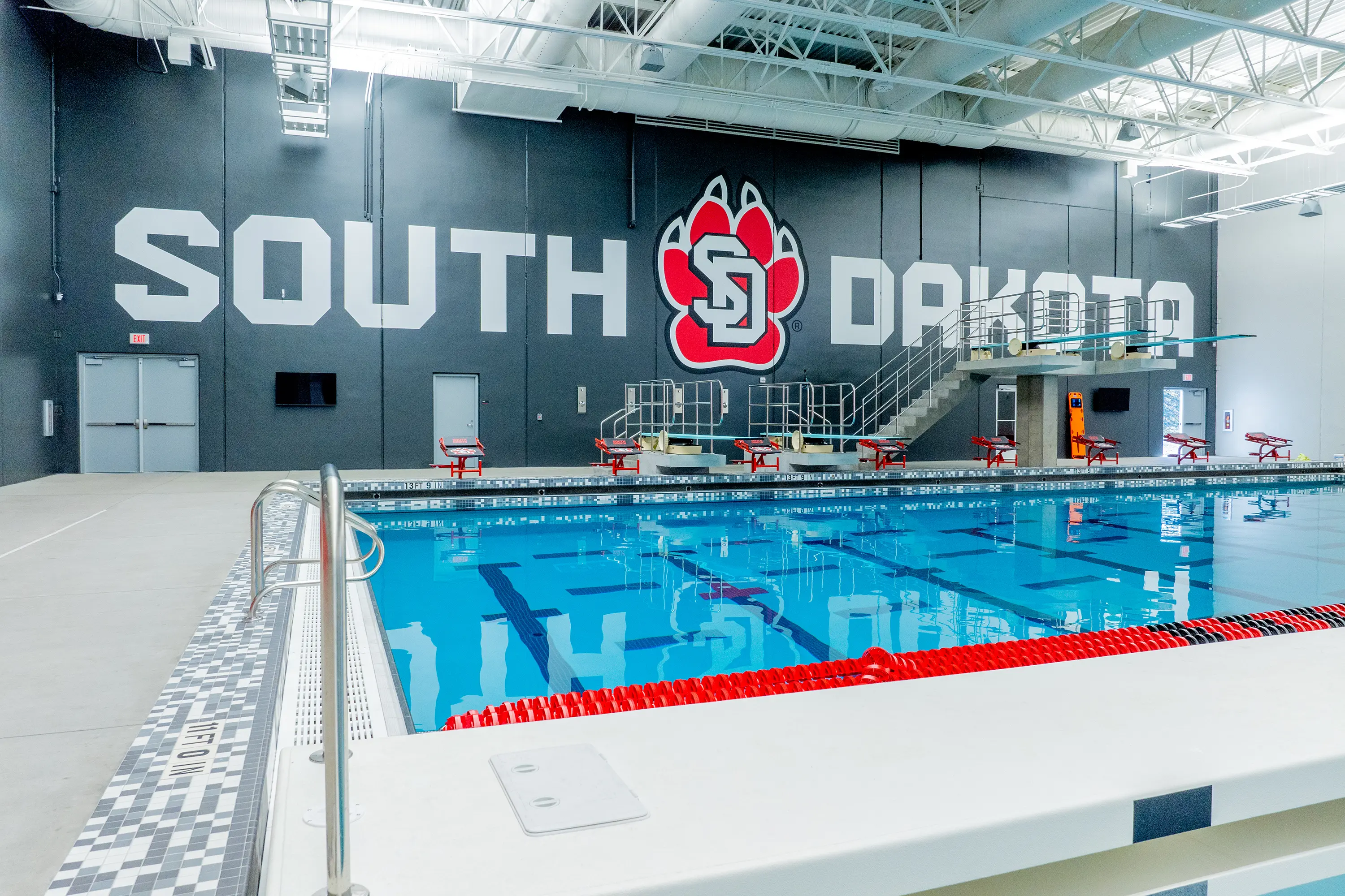 Usd Natatorium Wellness Center 38 Mid-pool view with South Dakota logo and diving boards above competition lanes.